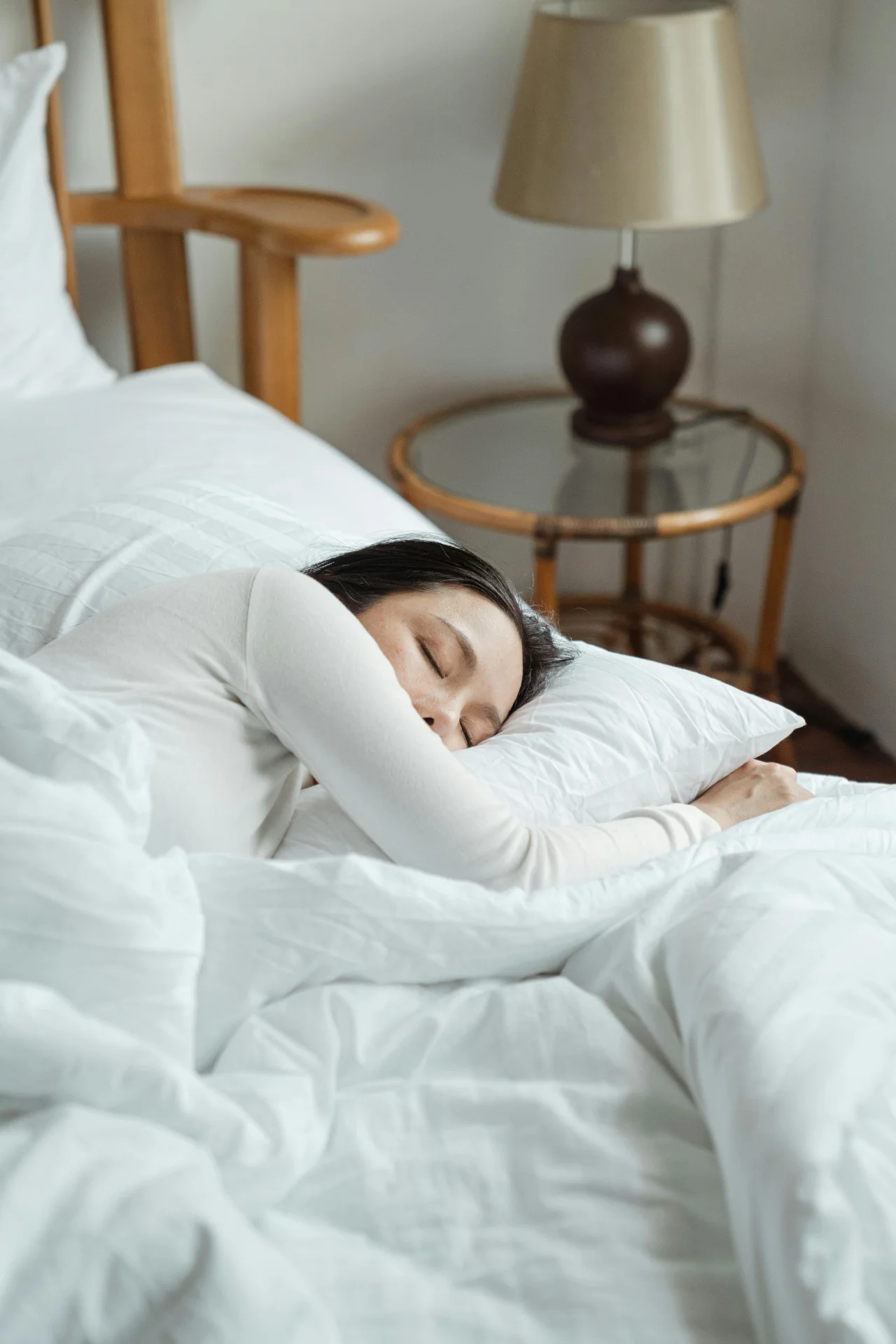 A woman peacefully sleeping in a bed with white linens.