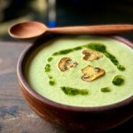 Creamy green soup with mushrooms in wooden bowl